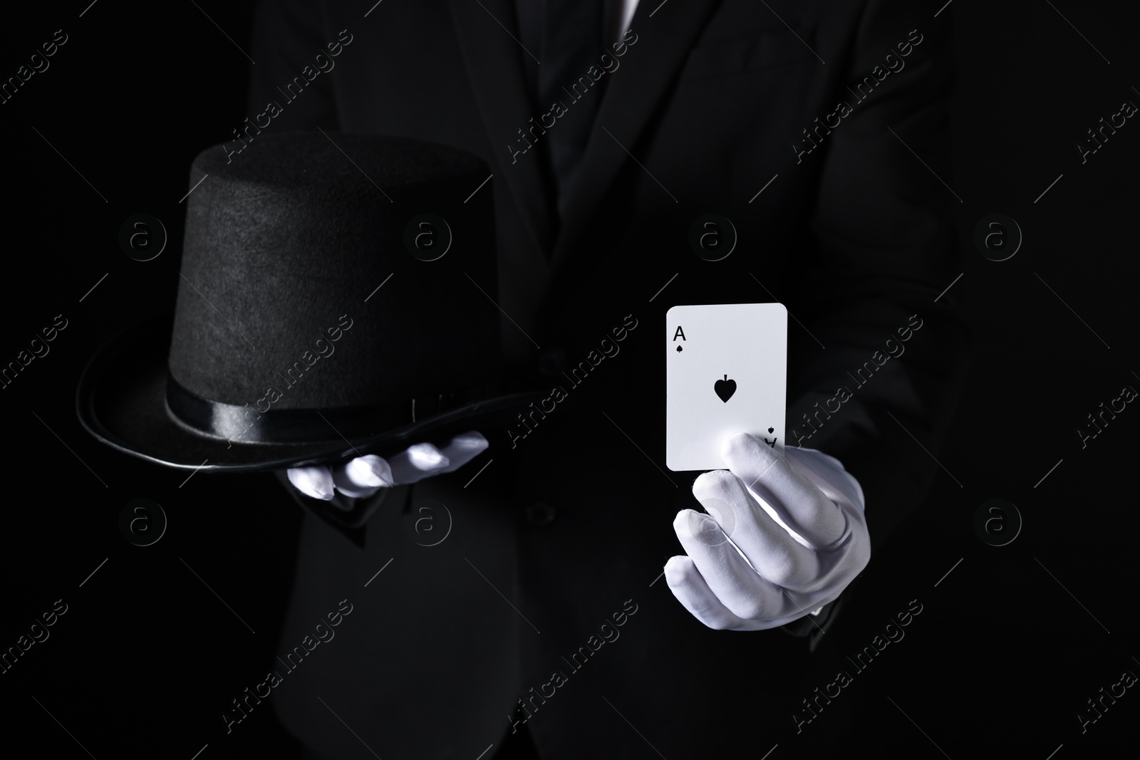 Photo of Illusionist with playing card and hat on black background, closeup