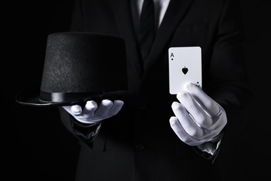 Photo of Illusionist with playing card and hat on black background, closeup