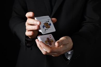 Photo of Illusionist shuffling playing cards on black background, closeup