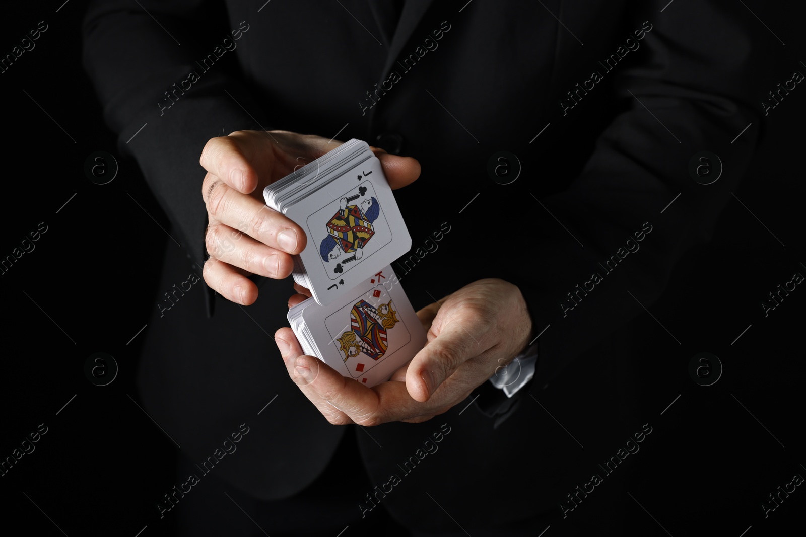 Photo of Illusionist shuffling playing cards on black background, closeup