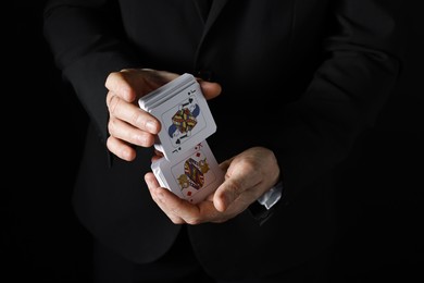 Photo of Illusionist shuffling playing cards on black background, closeup