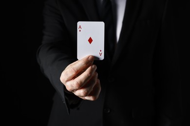 Photo of Illusionist with playing card on black background, closeup