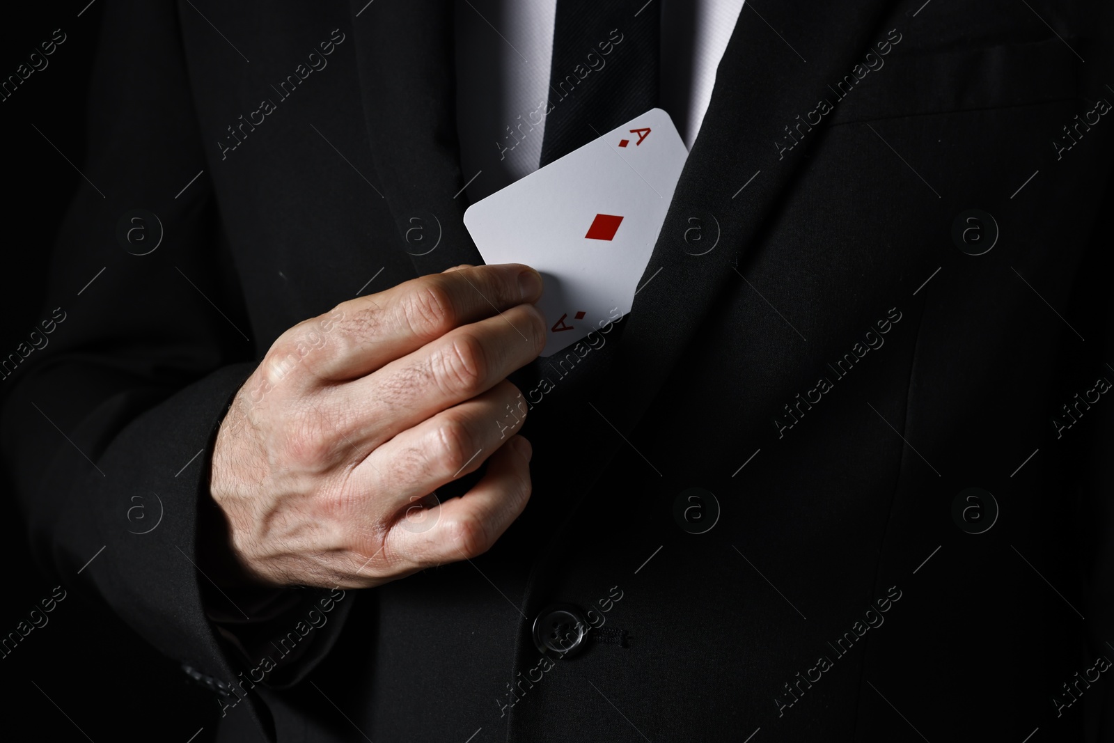 Photo of Illusionist hiding playing card behind jacket lapel on black background, closeup