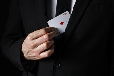 Photo of Illusionist hiding playing card behind jacket lapel on black background, closeup