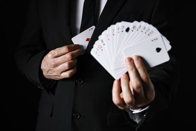 Photo of Illusionist hiding one playing card behind jacket lapel while showing deck on black background, selective focus