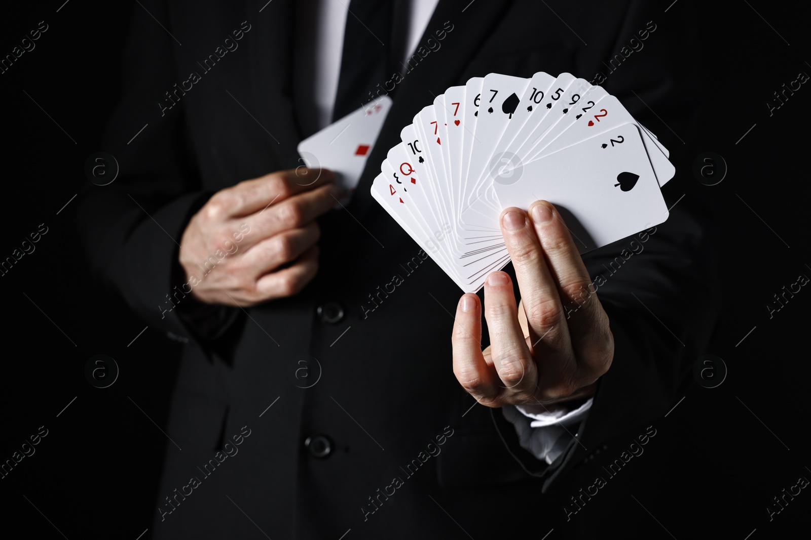 Photo of Illusionist hiding one playing card behind jacket lapel while showing deck on black background, selective focus