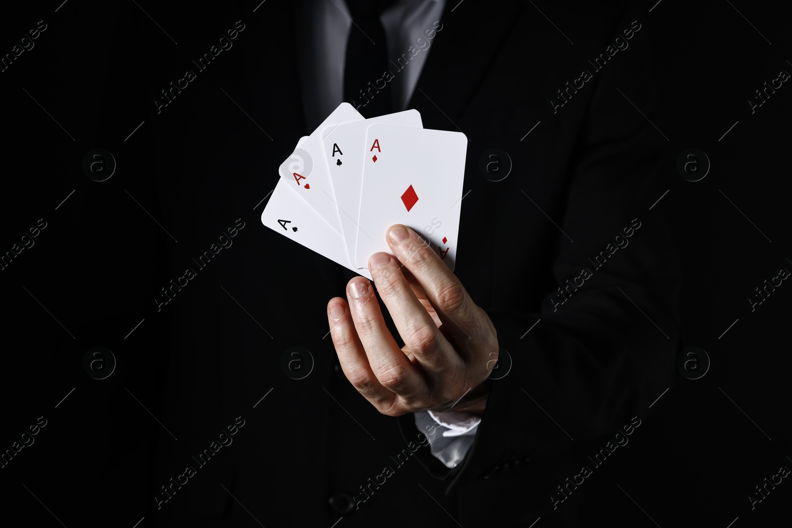 Photo of Illusionist with playing cards on black background, closeup