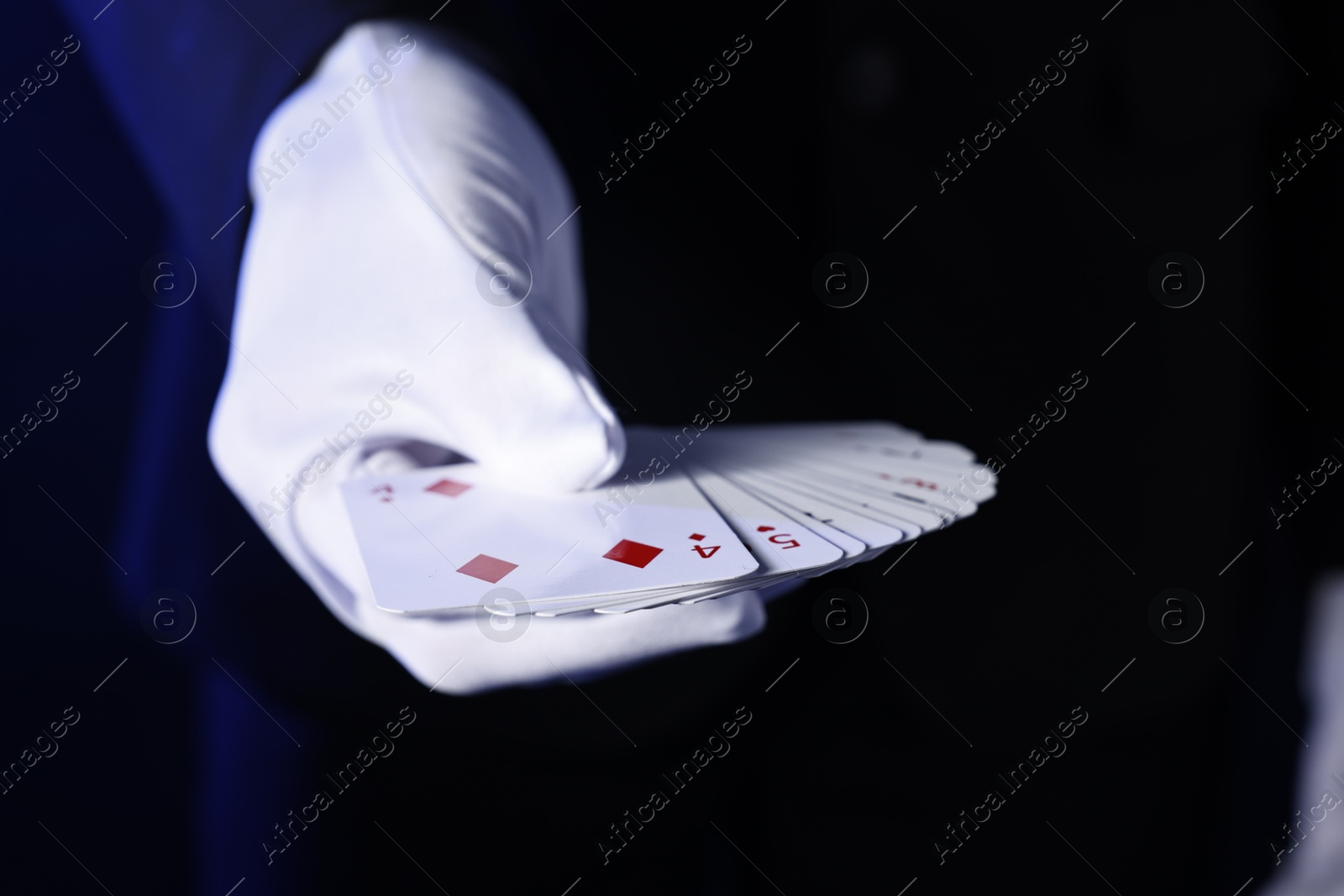 Photo of Illusionist with playing cards on dark blue background, closeup