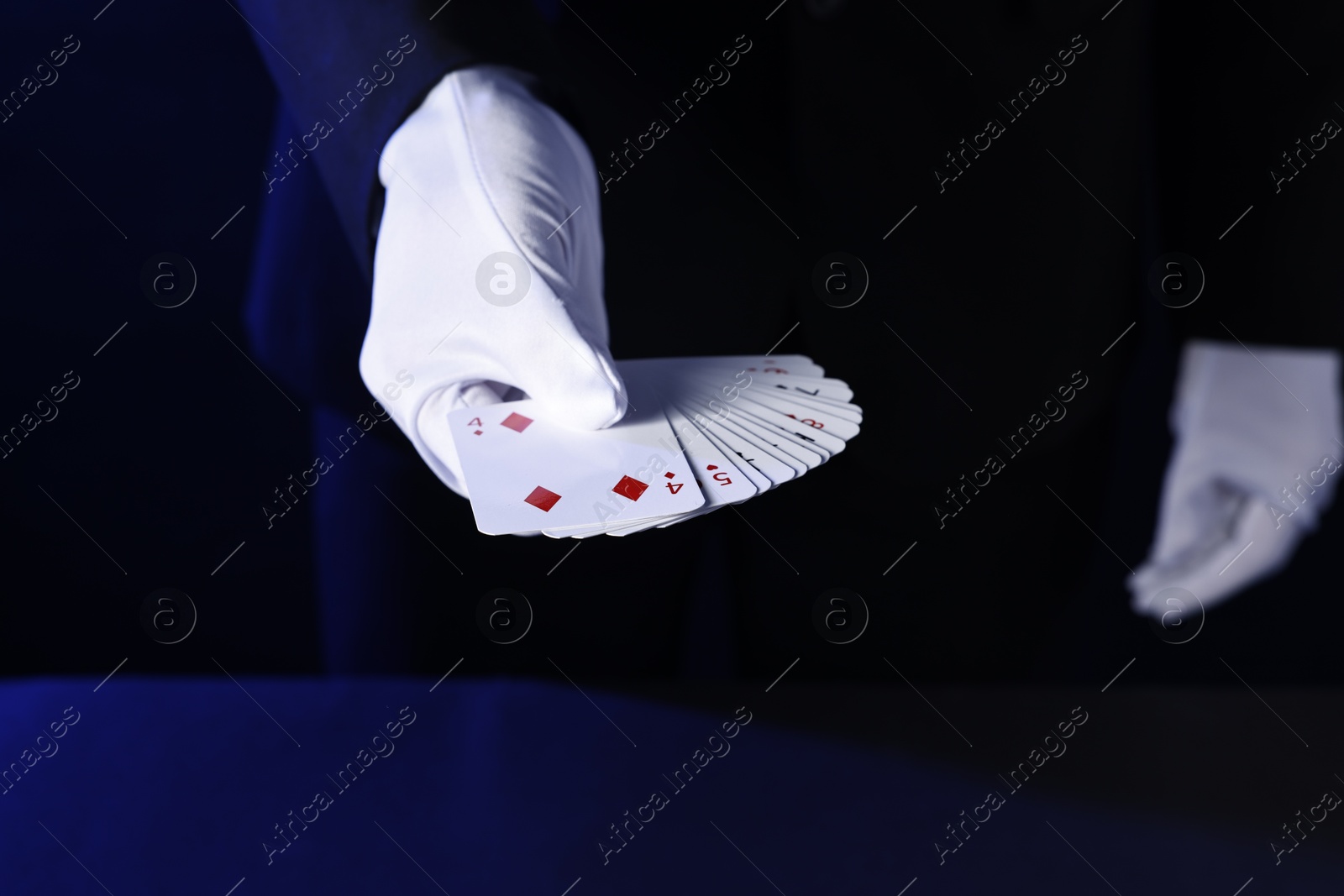 Photo of Illusionist with playing cards on dark blue background, closeup