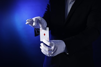 Photo of Illusionist with playing card on dark blue background, closeup