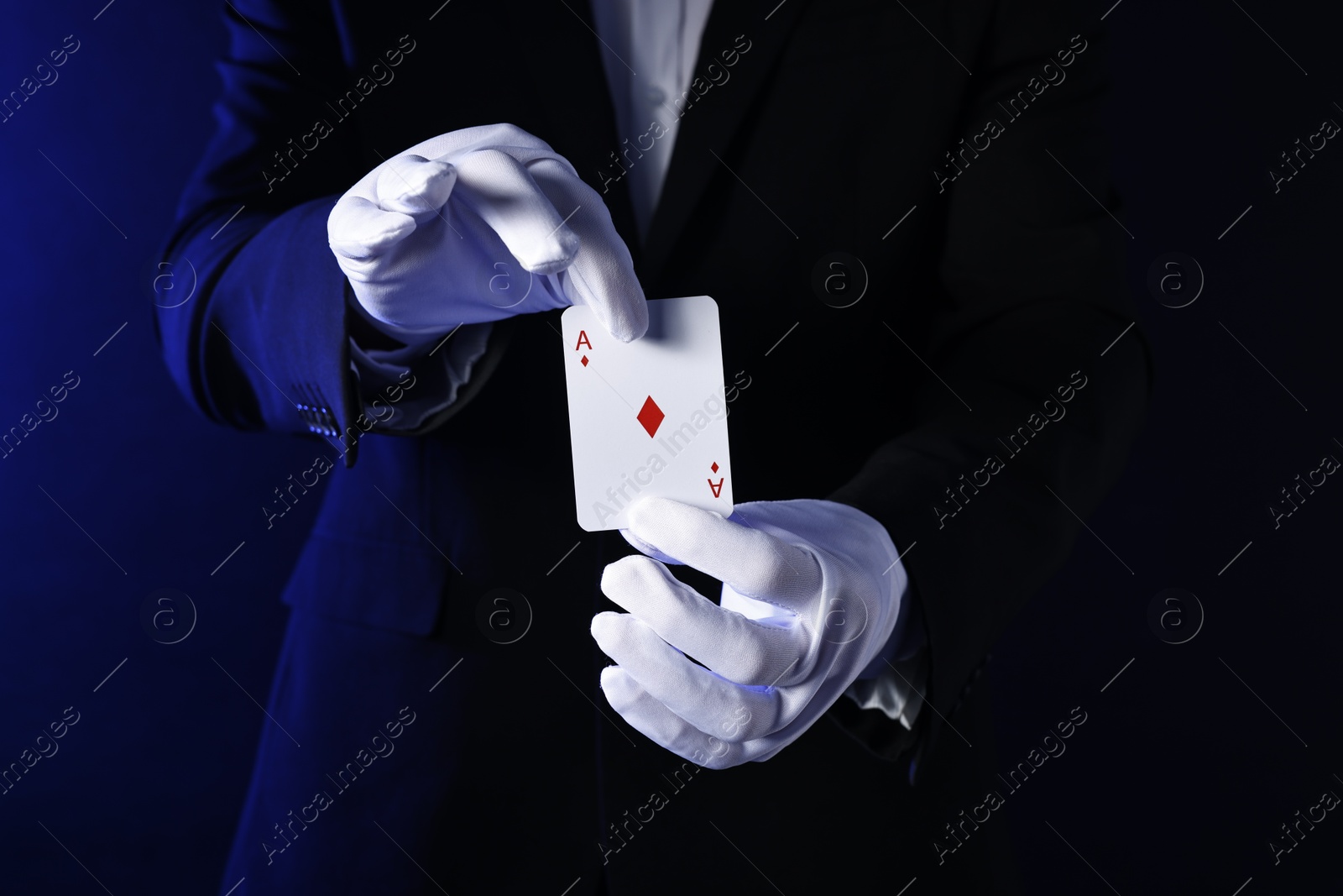 Photo of Illusionist with playing card on dark blue background, closeup