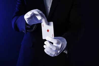 Photo of Illusionist with playing card on dark blue background, closeup