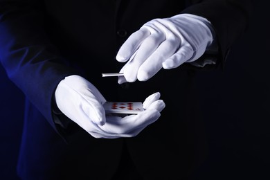 Photo of Illusionist shuffling playing cards on dark blue background, closeup