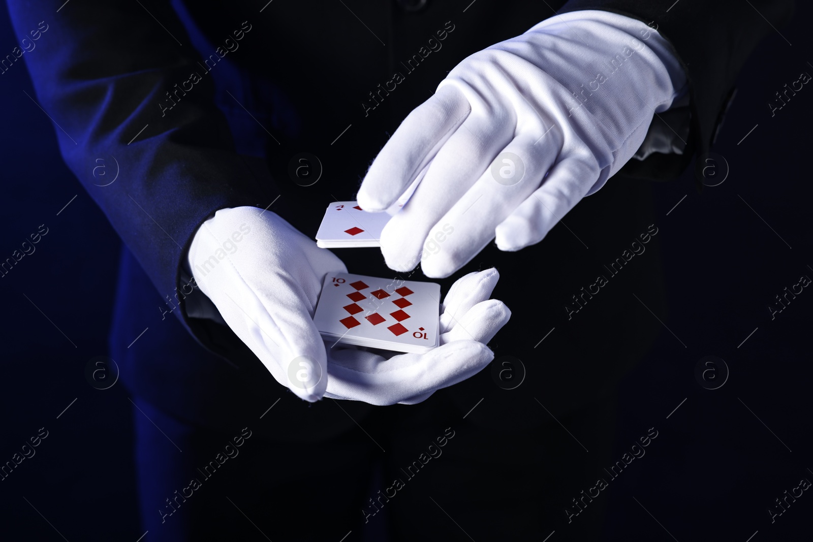 Photo of Illusionist shuffling playing cards on dark blue background, closeup