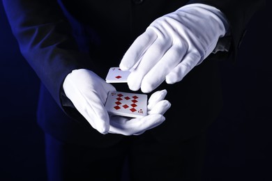 Photo of Illusionist shuffling playing cards on dark blue background, closeup