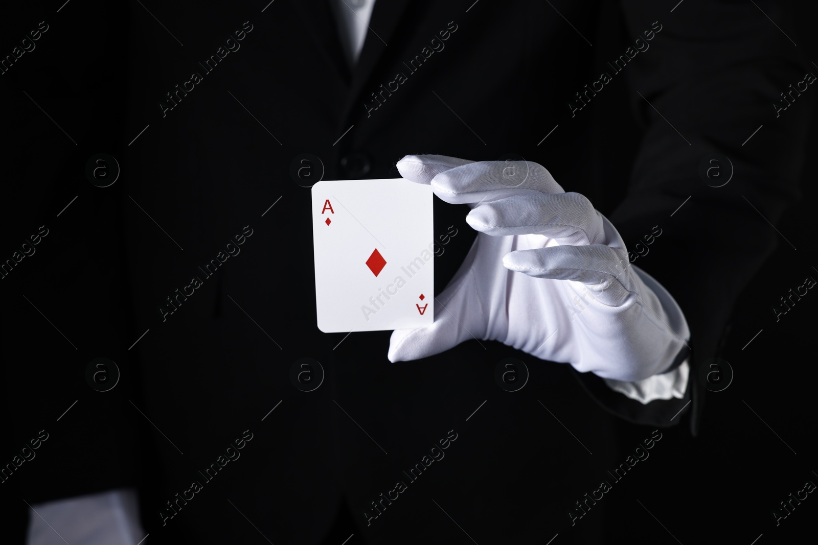 Photo of Illusionist with playing card on black background, closeup