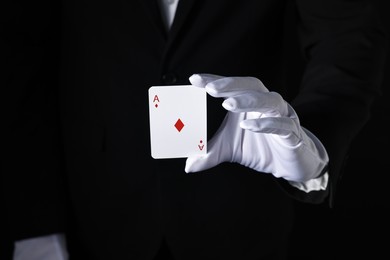 Illusionist with playing card on black background, closeup