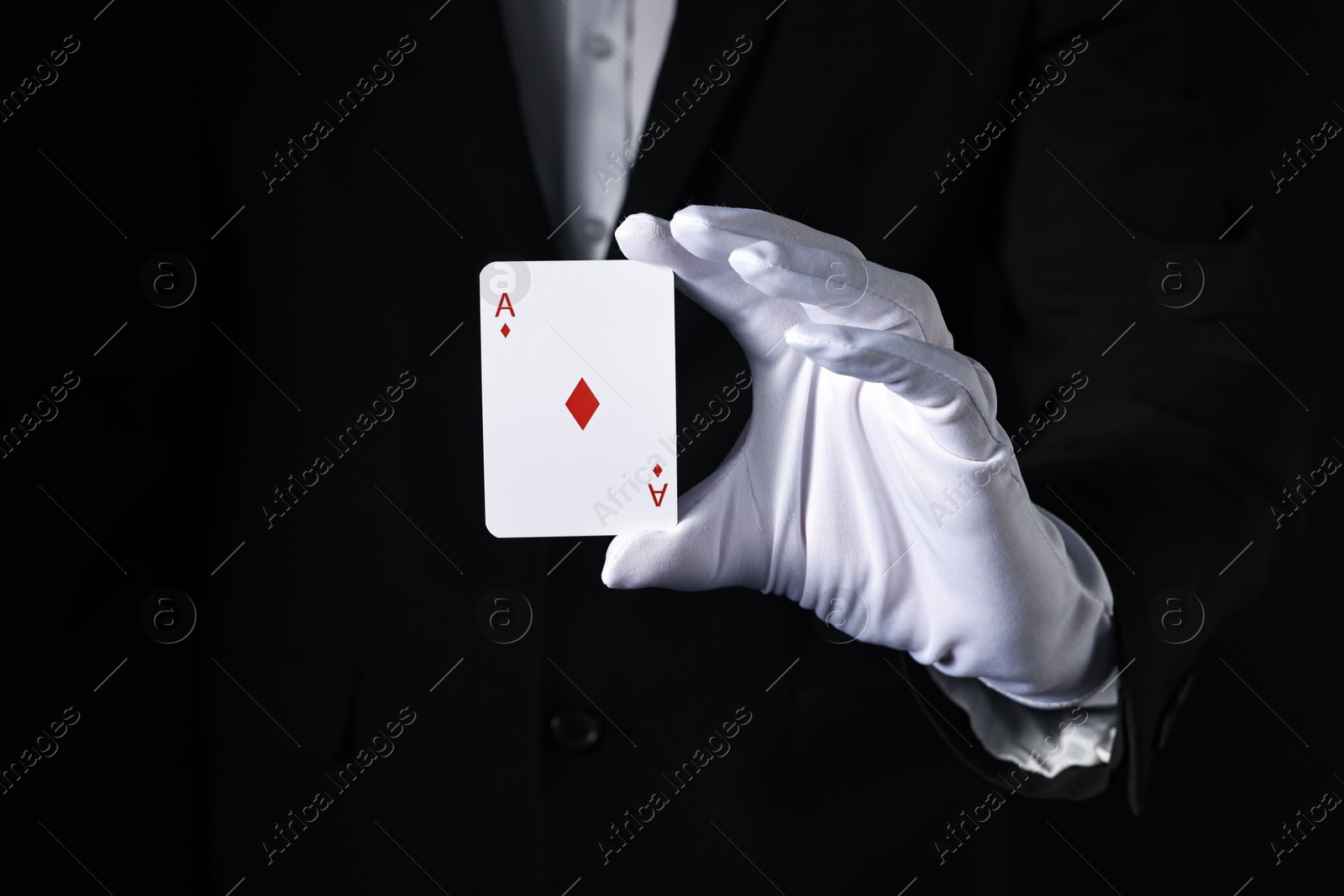 Photo of Illusionist with playing card on black background, closeup