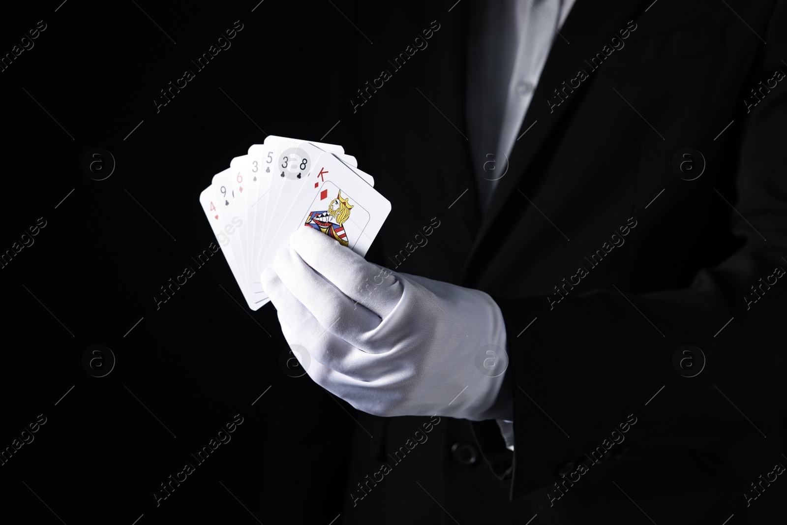 Photo of Illusionist with playing cards on black background, closeup