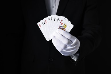 Photo of Illusionist with playing cards on black background, closeup