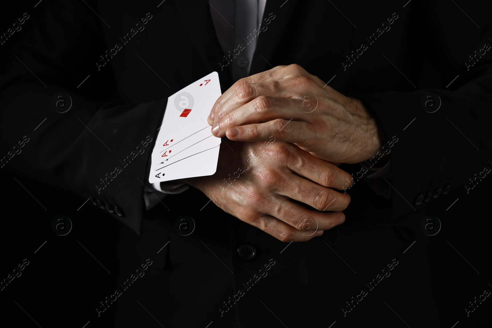 Photo of Illusionist taking playing cards out of sleeve on black background, closeup