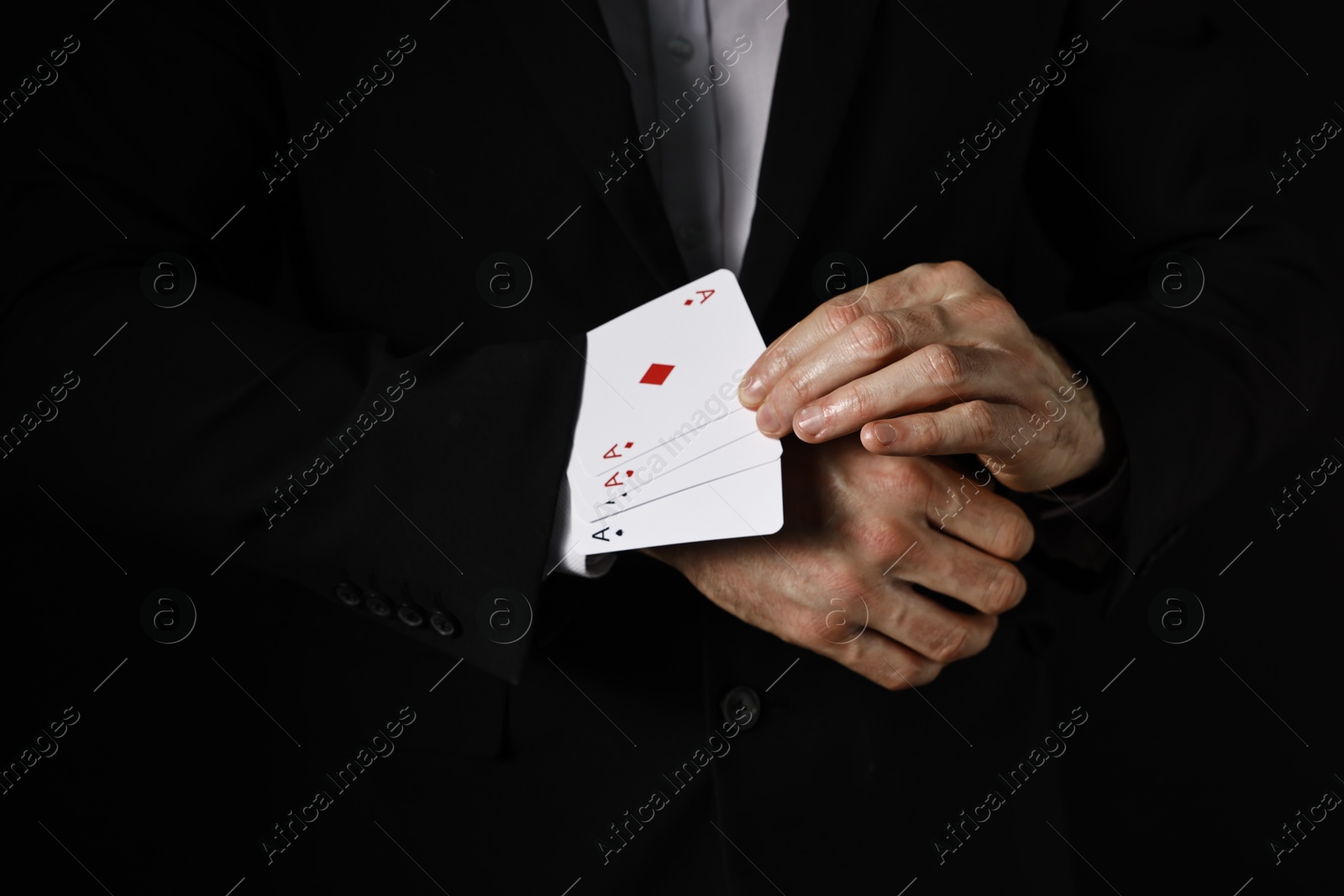 Photo of Illusionist taking playing cards out of sleeve on black background, closeup