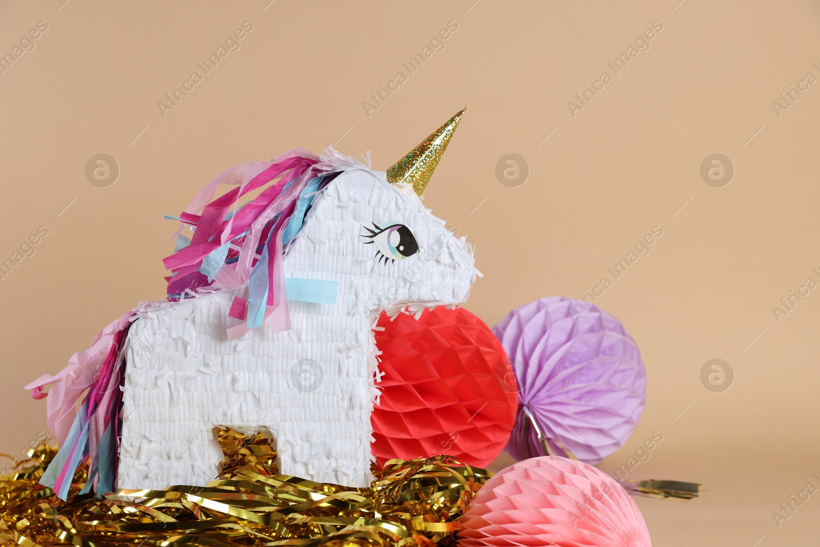 Photo of Unicorn shaped pinata and party decor on beige background, space for text