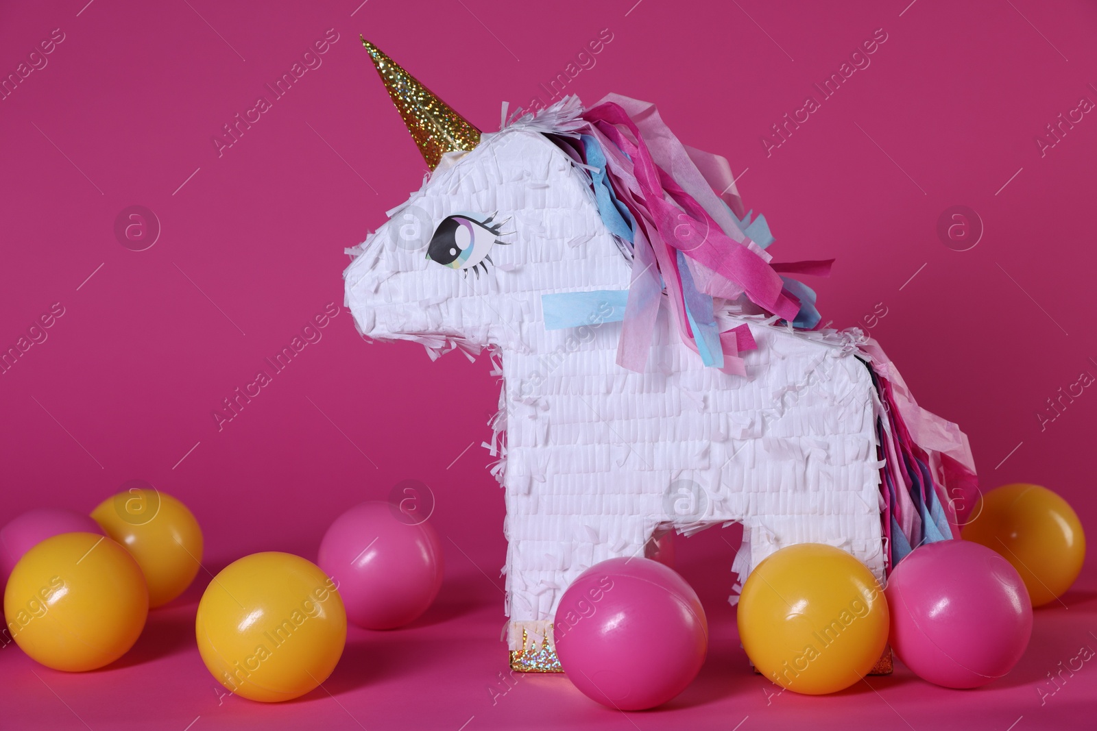 Photo of Unicorn shaped pinata and balls on bright pink background