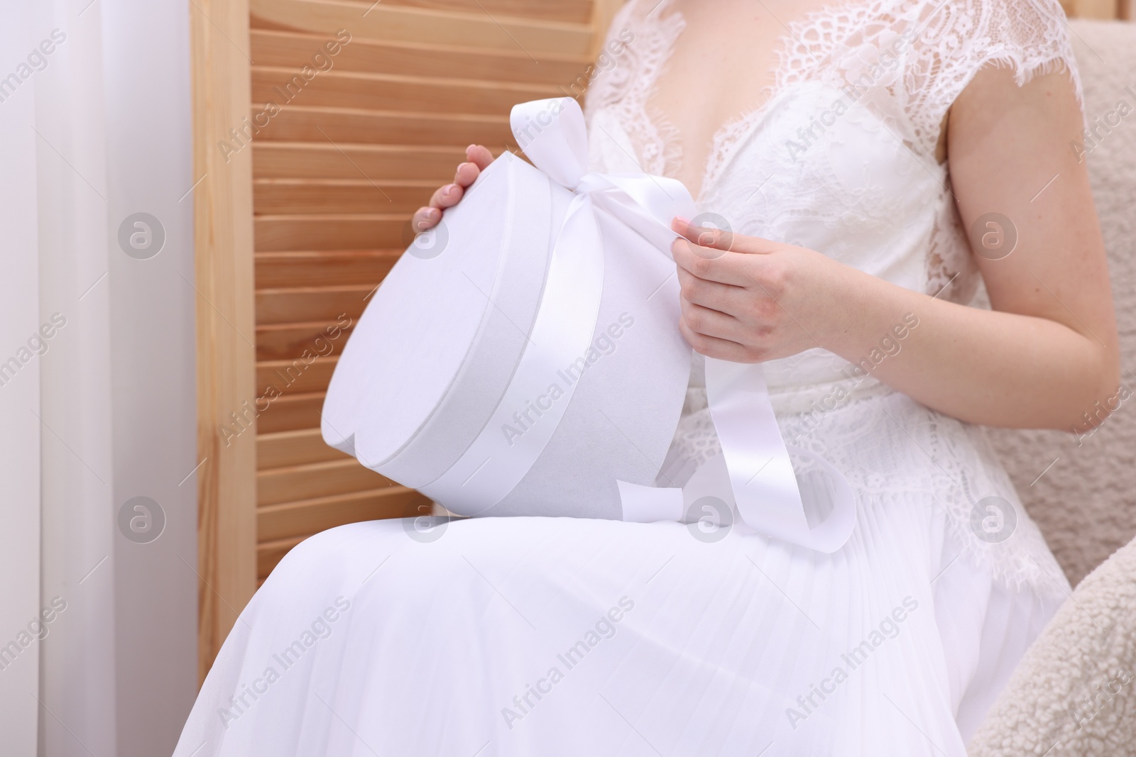 Photo of Bride opening beautiful wedding gift indoors, closeup