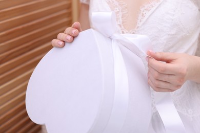 Photo of Bride opening beautiful wedding gift indoors, closeup