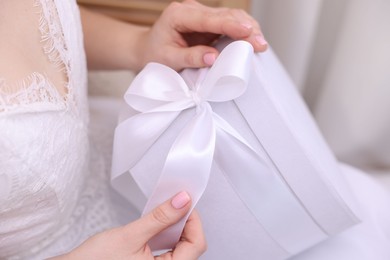 Photo of Bride opening beautiful wedding gift indoors, closeup