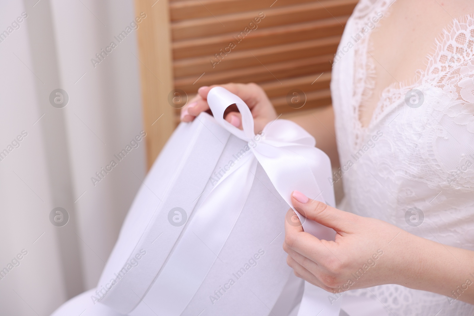 Photo of Bride opening beautiful wedding gift indoors, closeup