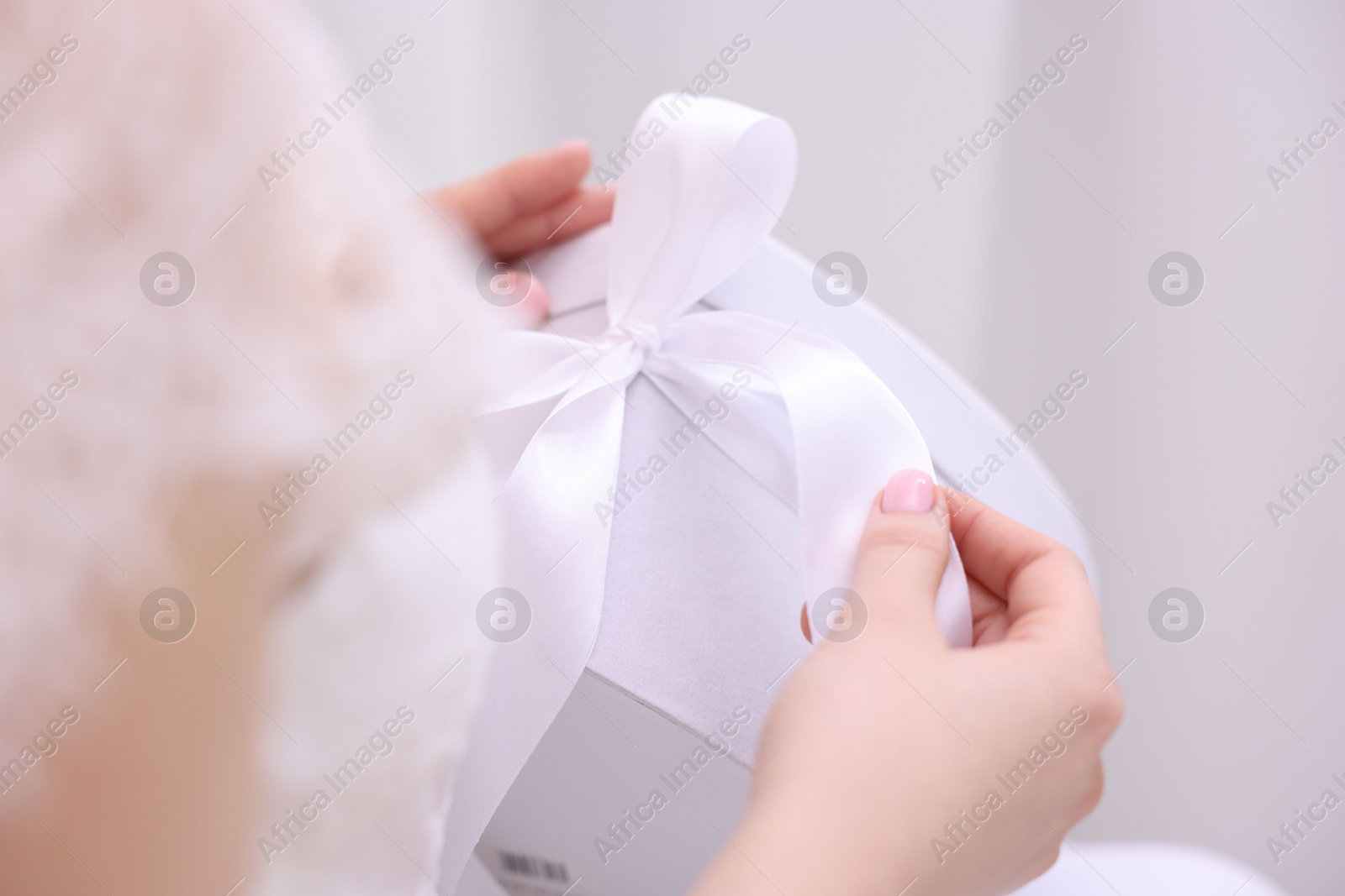 Photo of Bride opening beautiful wedding gift indoors, closeup