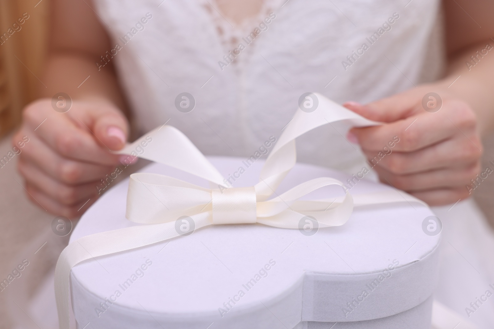 Photo of Bride opening beautiful wedding gift indoors, closeup