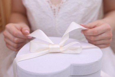 Photo of Bride opening beautiful wedding gift indoors, closeup