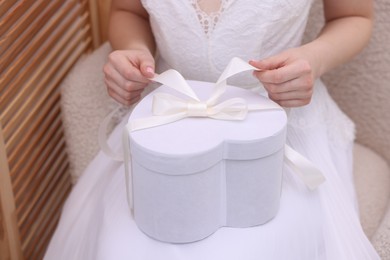 Photo of Bride opening beautiful wedding gift indoors, closeup