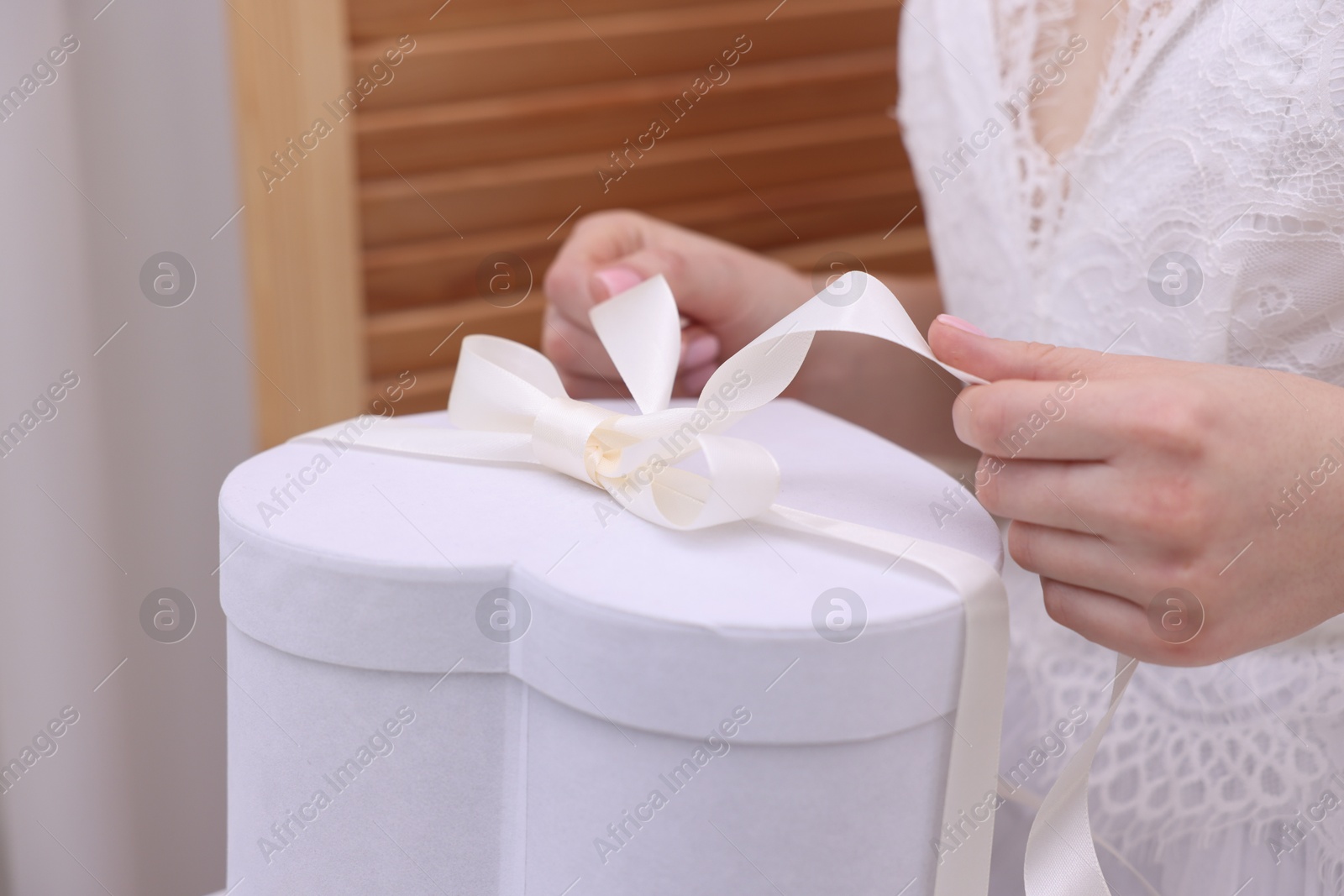 Photo of Bride opening beautiful wedding gift indoors, closeup