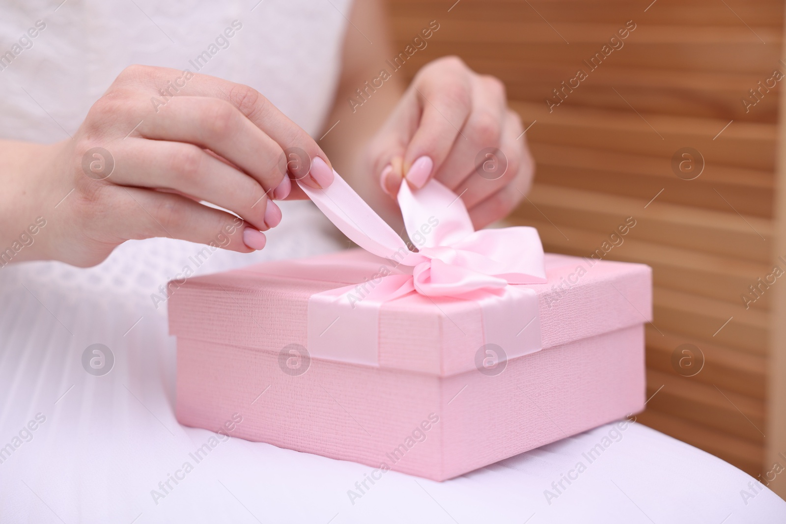 Photo of Bride opening beautiful wedding gift indoors, closeup