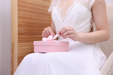 Photo of Bride opening beautiful wedding gift indoors, closeup