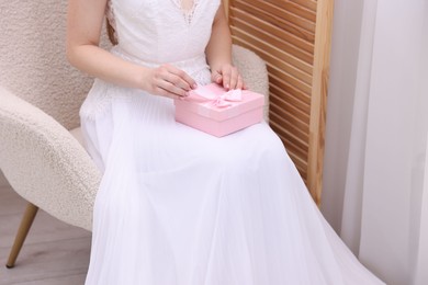 Photo of Bride opening beautiful wedding gift indoors, closeup