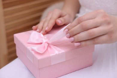 Photo of Bride opening beautiful wedding gift indoors, closeup