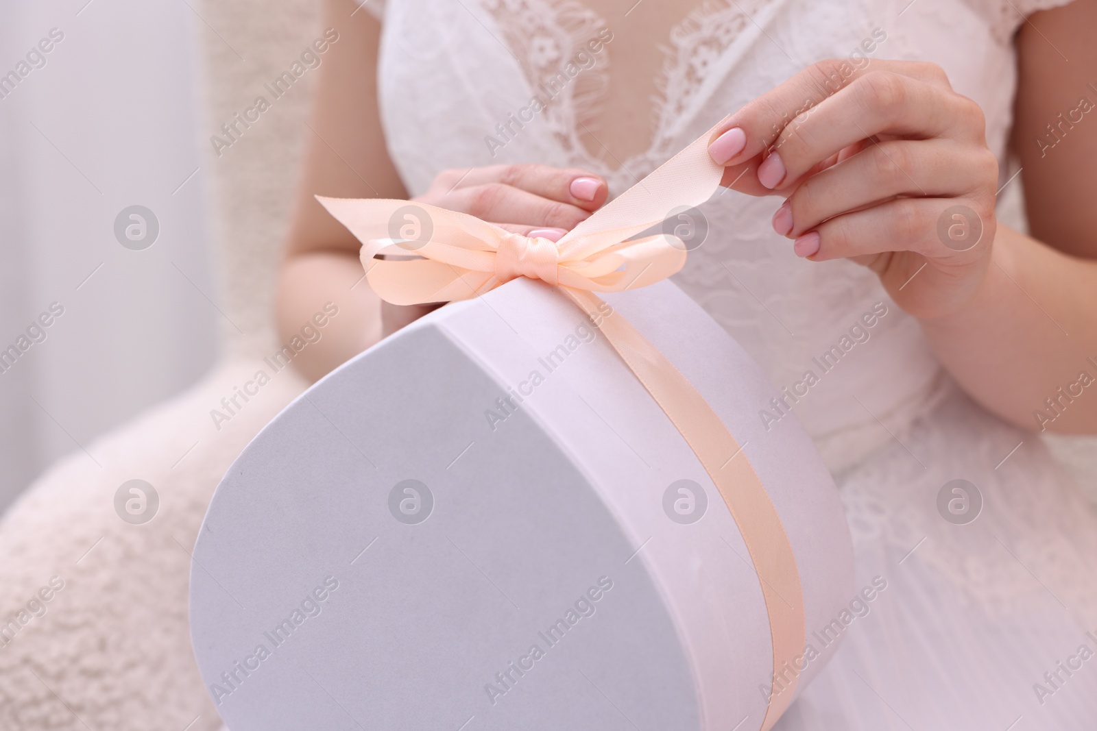 Photo of Bride opening beautiful wedding gift indoors, closeup