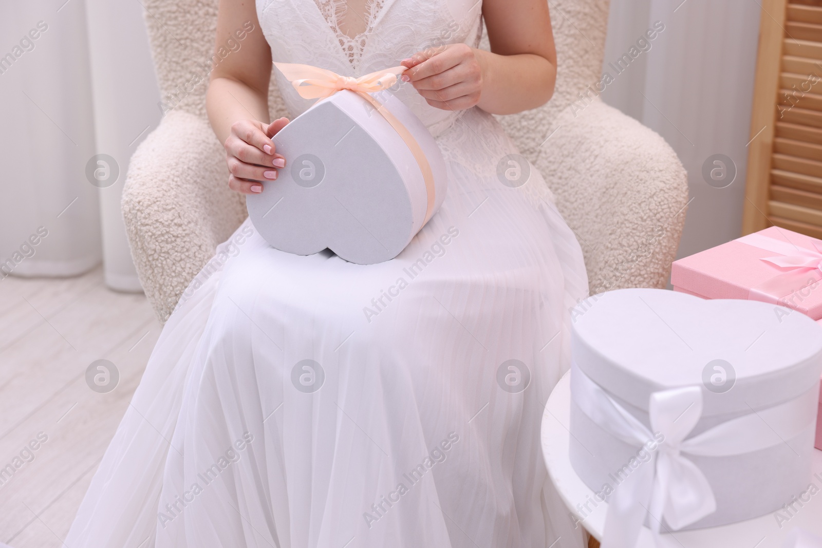 Photo of Bride opening beautiful wedding gift indoors, closeup