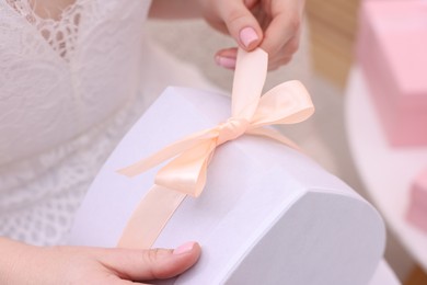 Photo of Bride opening beautiful wedding gift indoors, closeup