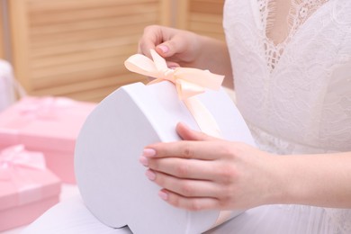 Photo of Bride opening beautiful wedding gift indoors, closeup