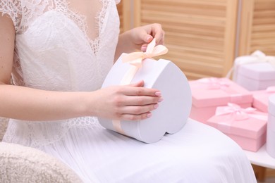 Photo of Bride opening beautiful wedding gift indoors, closeup