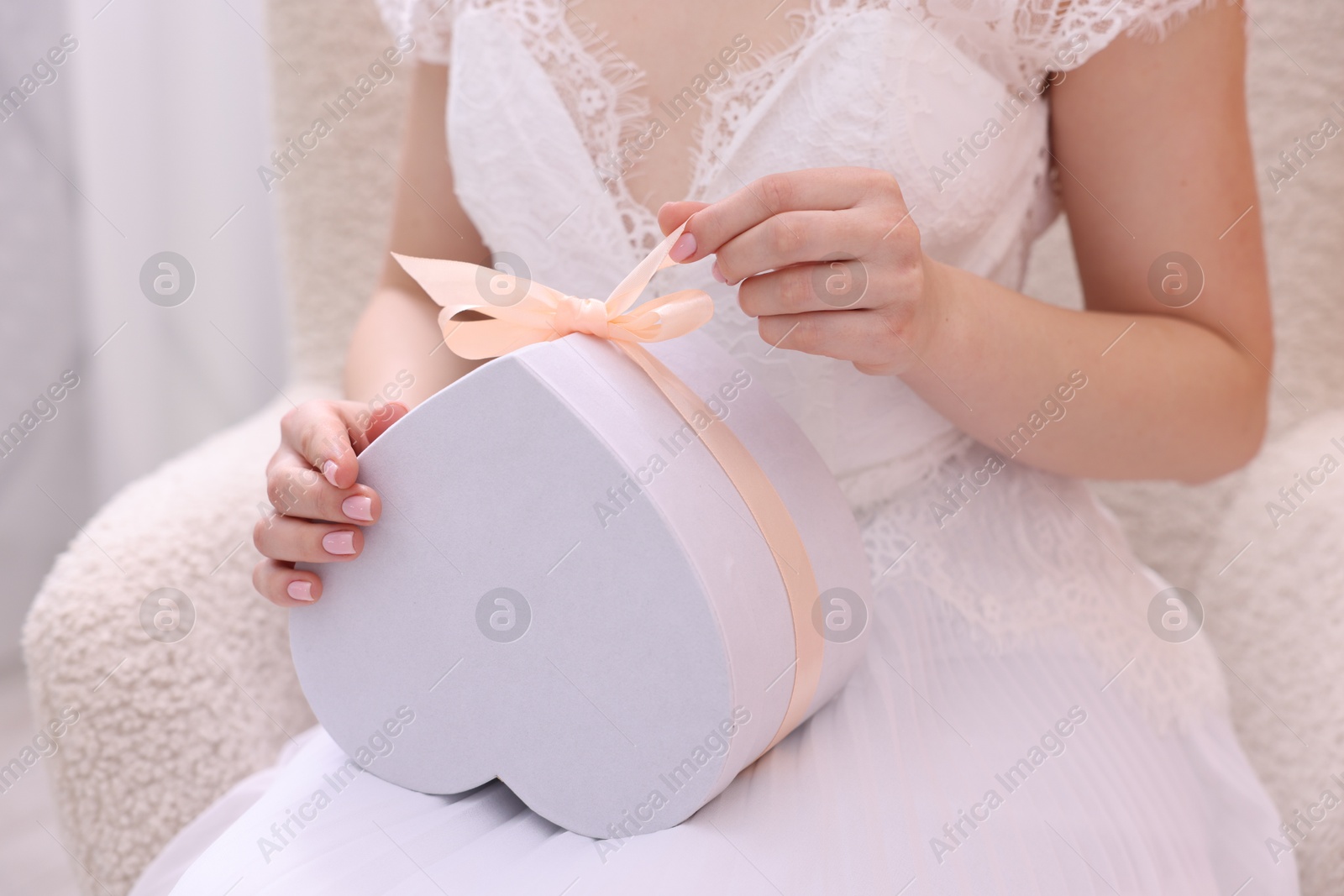 Photo of Bride opening beautiful wedding gift indoors, closeup