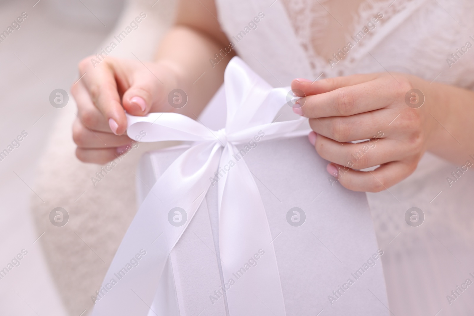 Photo of Bride opening beautiful wedding gift indoors, closeup