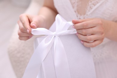 Photo of Bride opening beautiful wedding gift indoors, closeup