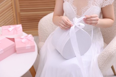 Photo of Bride opening beautiful wedding gift indoors, closeup